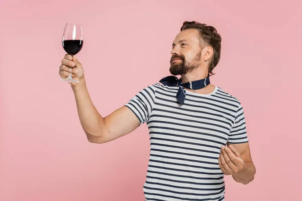 Homem alegre em listrado t-shirt segurando vidro de vinho francês vermelho isolado em rosa — Fotografia de Stock