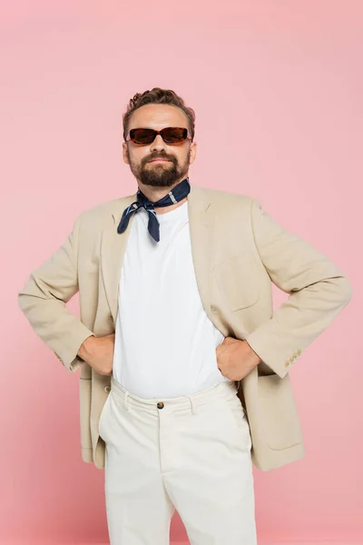 Elegante francese uomo in sciarpa collo e occhiali da sole in posa con le mani sui fianchi isolati su rosa — Foto stock