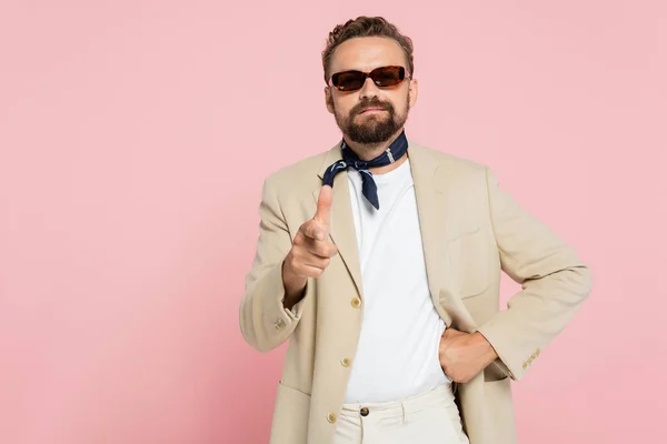 Elegante ragazzo francese in sciarpa collo e occhiali da sole che punta alla fotocamera isolata su rosa — Foto stock