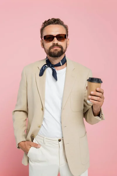 Elegante hombre francés en la bufanda del cuello y gafas de sol sosteniendo café para ir aislado en rosa - foto de stock