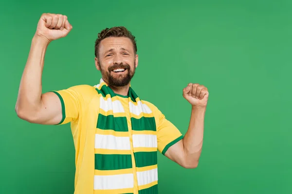 Fanático de los deportes emocionados en bufanda a rayas y camiseta amarilla mirando a la cámara aislada en verde - foto de stock