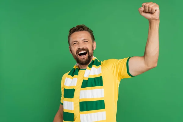 Емоційний спортивний вентилятор в смугастому шарфі і жовта футболка радіє ізольовано на зеленому — стокове фото