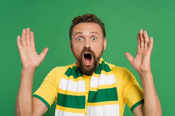 Шокований спортивний вентилятор в смугастому шарфі і жовта футболка кричить ізольовано на зеленому — стокове фото