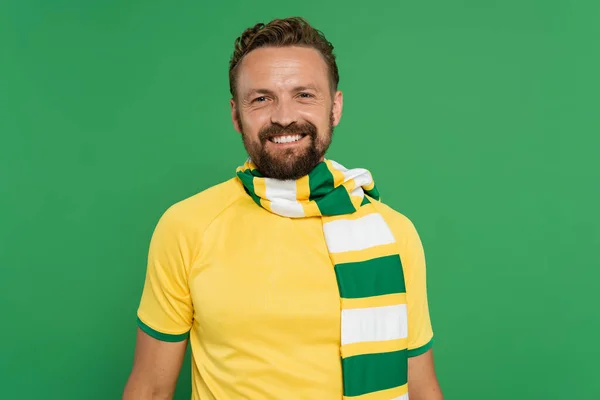 Tifoso sportivo positivo in sciarpa a righe e t-shirt gialla guardando la fotocamera isolata sul verde — Foto stock