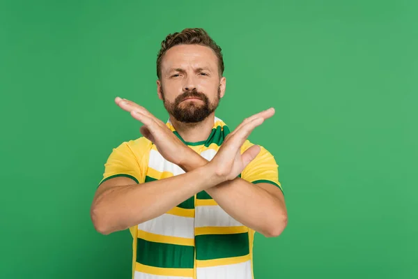 Éventail de football barbu en écharpe rayée et t-shirt jaune montrant geste d'arrêt avec les mains isolées sur vert — Photo de stock