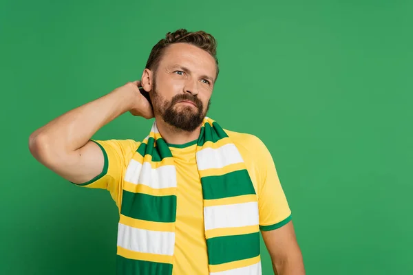 Fã de futebol pensativo em cachecol listrado e camiseta amarela olhando para longe isolado em verde — Fotografia de Stock