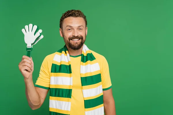 Весёлый футбольный болельщик в полосатом шарфе с пластиковой рукояткой, изолированной на зелёном — стоковое фото