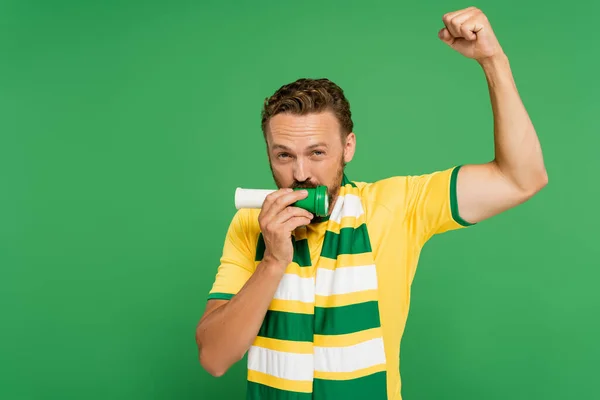 Бородатий спортивний вентилятор в шарфі дме ріг, підбадьорюючи ізольований на зеленому — стокове фото