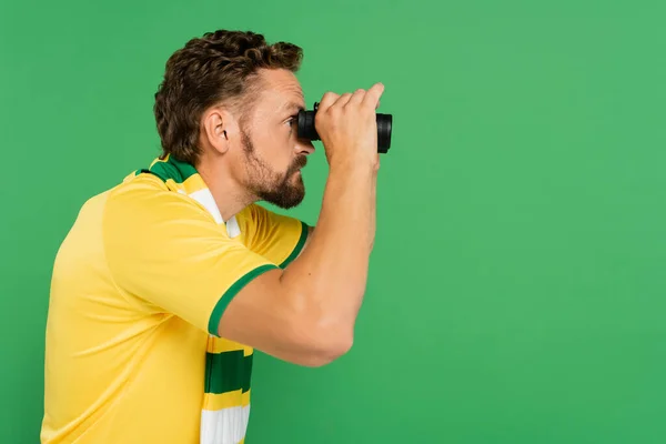 Seitenansicht eines bärtigen Mannes in gestreiftem Schal mit Fernglas während eines Fußballspiels isoliert auf grün — Stockfoto