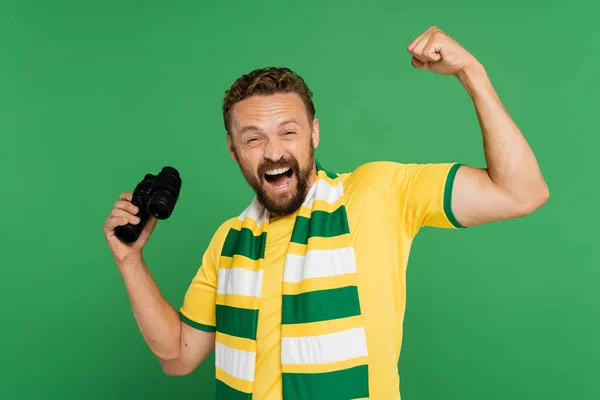 Uomo eccitato in sciarpa a righe che tiene binocolo durante la partita di calcio isolato sul verde — Foto stock