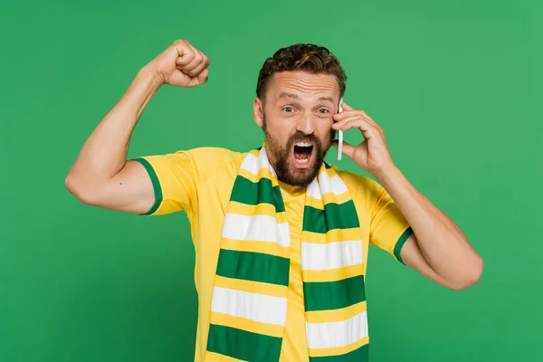 Эмоциональный мужчина в полосатом шарфе кричит во время разговора на мобильном телефоне изолирован на зеленый — стоковое фото