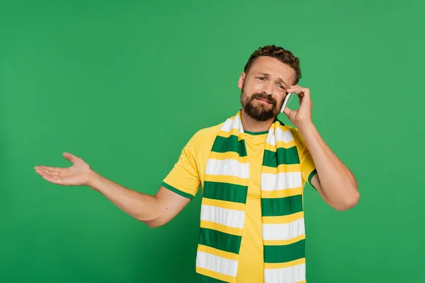 Недовольный мужчина в полосатом шарфе разговаривает на мобильном телефоне изолирован на зеленый — стоковое фото
