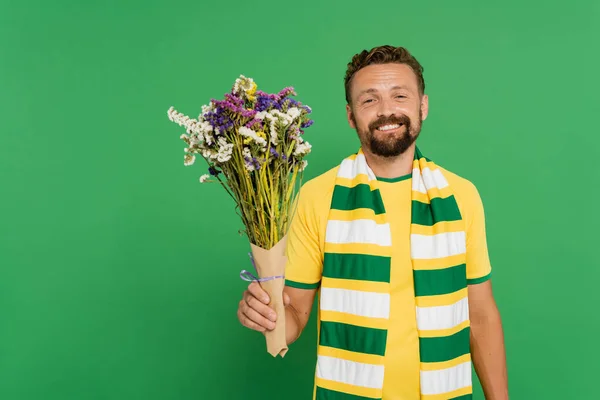 Happy bearded football fan holding wildflowers isolated on green — Stock Photo