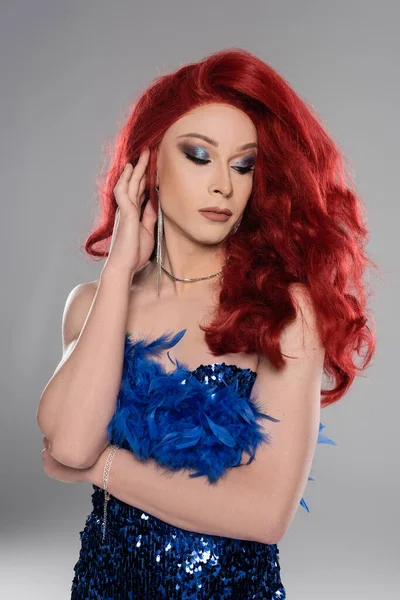 Портрет елегантної трансгендерної людини в сукні, що торкається червоного перуки ізольовано на сірому — стокове фото