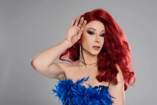 Retrato de drag queen en peluca roja mirando a la cámara aislada en gris - foto de stock