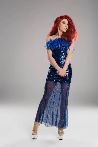 Volle Länge der lächelnden Drag Queen im blauen Kleid, die vor grauem Hintergrund wegschaut — Stockfoto