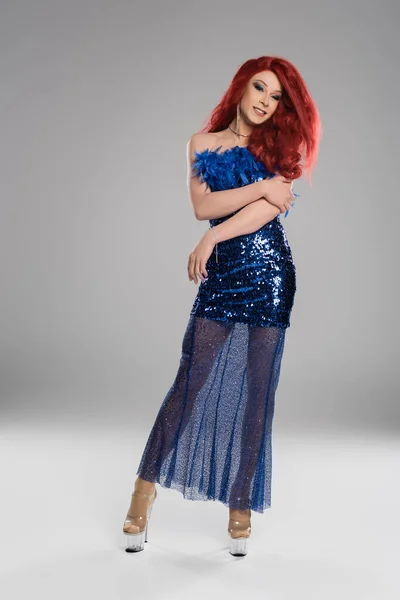 Volle Länge der lächelnden Drag Queen im blauen Kleid mit Federn auf grauem Hintergrund — Stockfoto