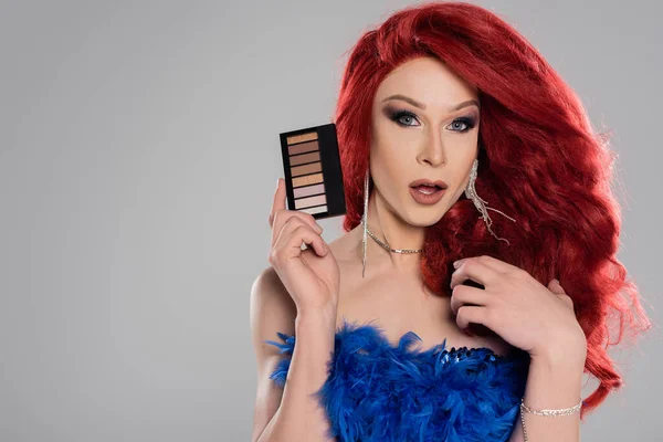 Transgender-Person mit roter Perücke hält Lidschatten isoliert auf grau — Stockfoto
