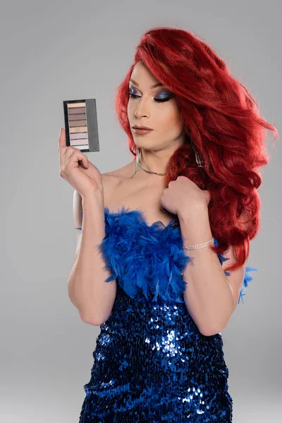 Elegant drag queen in dress holding eye shadows palette isolated on grey — Stock Photo