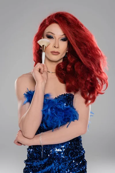 Portrait of drag queen in wig and dress holding makeup brush isolated on grey — Stock Photo