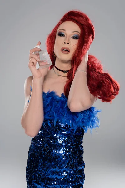 Portrait of elegant drag queen looking at camera and holding perfume isolated on grey — Stock Photo