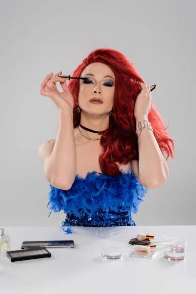 Fashionable drag queen applying mascara near decorative cosmetics isolated on grey — Stock Photo