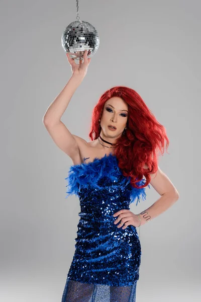 Elegant drag queen in dress touching disco ball and posing isolated on grey — Stock Photo