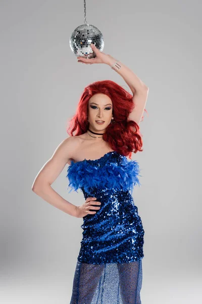 Despreocupada drag queen en vestido azul con plumas tocando la bola disco aislada en gris - foto de stock