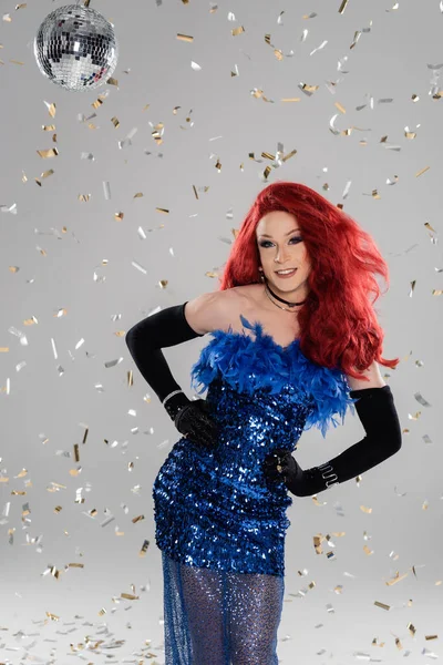 Sorrindo drag queen em luvas e vestido de pé sob bola de discoteca e confete no fundo cinza — Fotografia de Stock