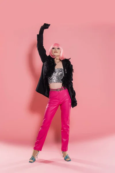 Full length of stylish drag queen in jacket with feathers posing on pink background — Stock Photo