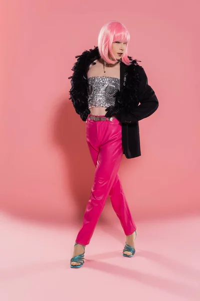 Lunghezza completa di elegante drag queen in giacca e top lucido camminare su sfondo rosa — Foto stock
