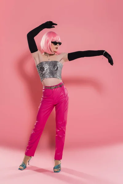 Full length of trendy drag queen in sparkling top and wig posing on pink background — Stock Photo