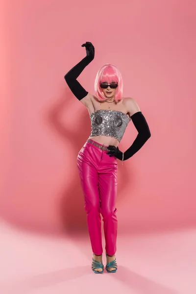 Moda drag queen en guantes y la parte superior brillante posando y mirando a la cámara sobre fondo rosa - foto de stock