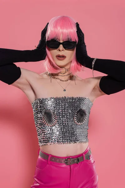 Trendy drag queen in sunglasses and gloves touching wig on pink background — Stock Photo