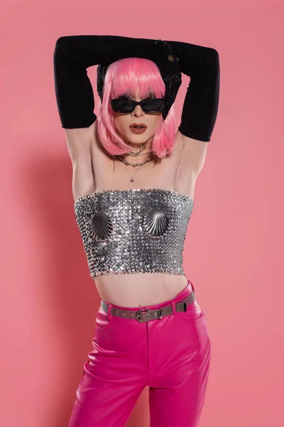 Modische Drag Queen mit Sonnenbrille und glänzendem Top, das die Haare auf rosa Hintergrund berührt — Stockfoto