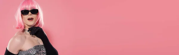 Возбужденный трансвестит в солнцезащитных очках и парике стоя на розовом фоне, баннер — стоковое фото