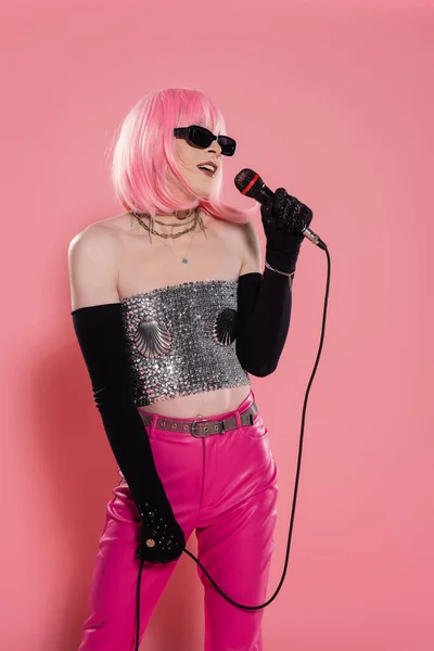 Drag queen in sunglasses and sparkling top holding microphone on pink background — Stock Photo