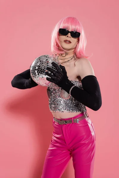 Moda drag queen en gafas de sol y guantes que sostienen la bola disco sobre fondo rosa - foto de stock