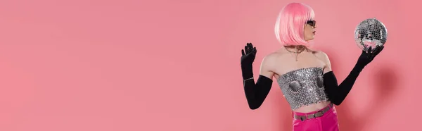 Side view of stylish drag queen in shiny top and gloves holding disco ball on pink background, banner — Stock Photo