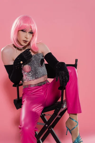 Модная королева драга в перчатках и топе, сидящая на стуле на розовом фоне — стоковое фото
