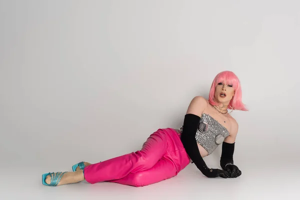 Trendy transgender person in sparkling top and gloves lying on grey background — Stock Photo
