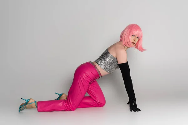 Drag queen tendance en perruque rose et haut regardant la caméra sur fond gris — Photo de stock