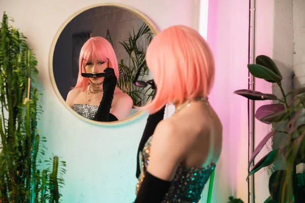 Desfocada drag queen na peruca usando óculos de sol perto do espelho em casa — Fotografia de Stock