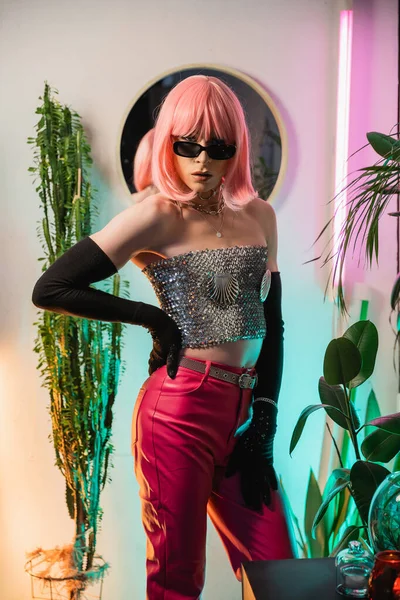 Moda drag queen en peluca rosa y top brillante posando en casa - foto de stock