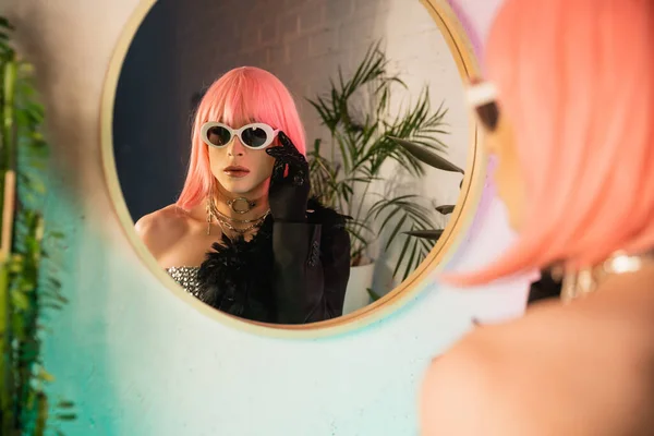 Desfocada drag queen em peruca rosa usando óculos de sol perto do espelho em casa — Fotografia de Stock