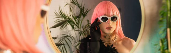 Moda drag queen en peluca rosa con gafas de sol cerca del espejo en casa, pancarta - foto de stock