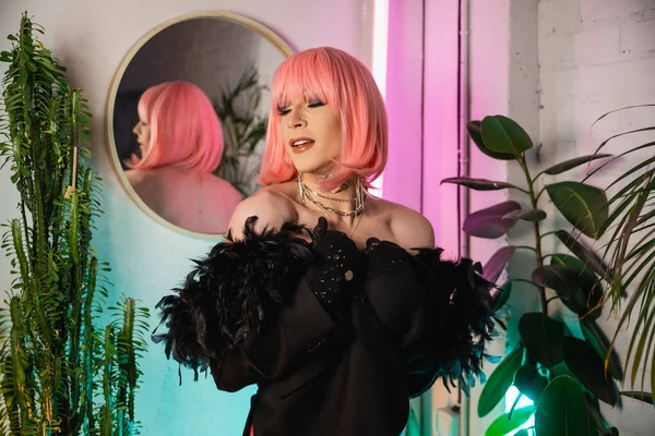 Transgender-Person mit pinkfarbener Perücke und Jacke steht bei Pflanzen zu Hause — Stockfoto