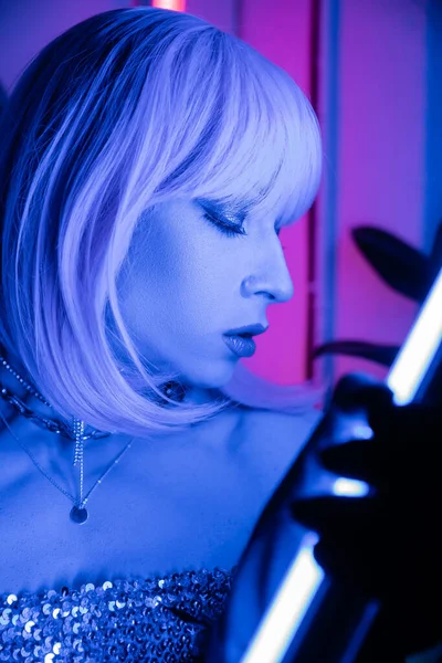 Portrait of drag queen in wig holding neon lamp at home — Stock Photo