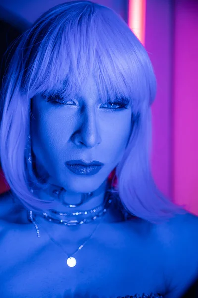Ritratto di drag queen in parrucca guardando la fotocamera in luce al neon a casa — Foto stock