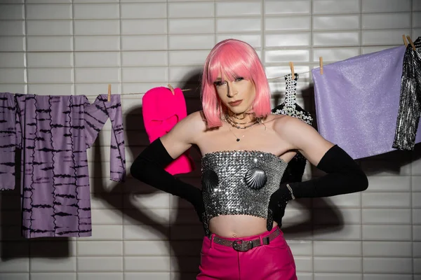 Stylish drag queen in wig posing near clothes on rope in bathroom — Stock Photo